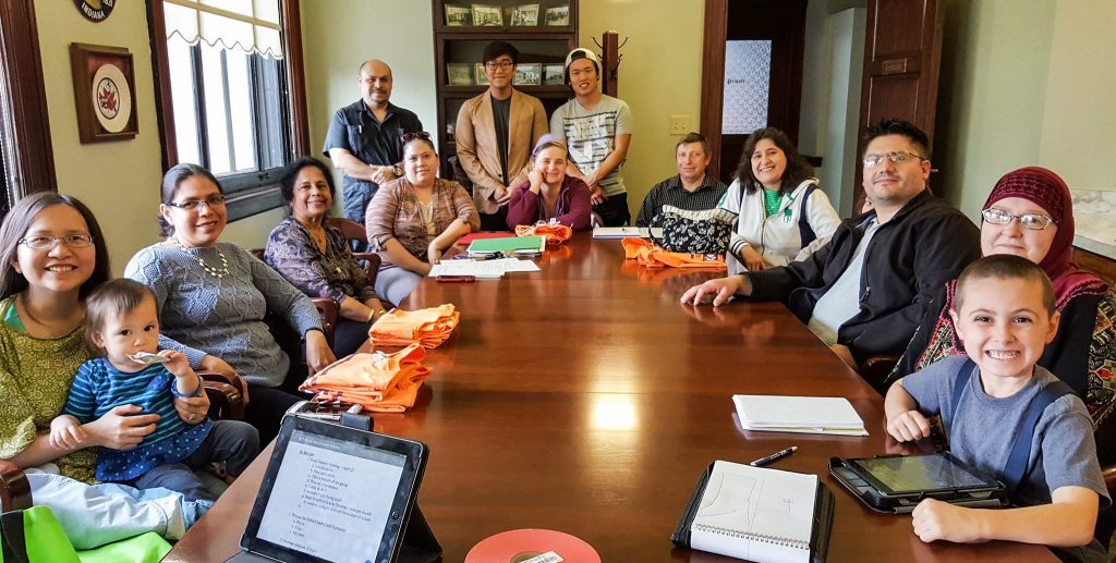 A group of people (women, men and children of diverse backgrounds), pose for a picture during a CRC meeting at the Goshen City Hall Conference Room. 