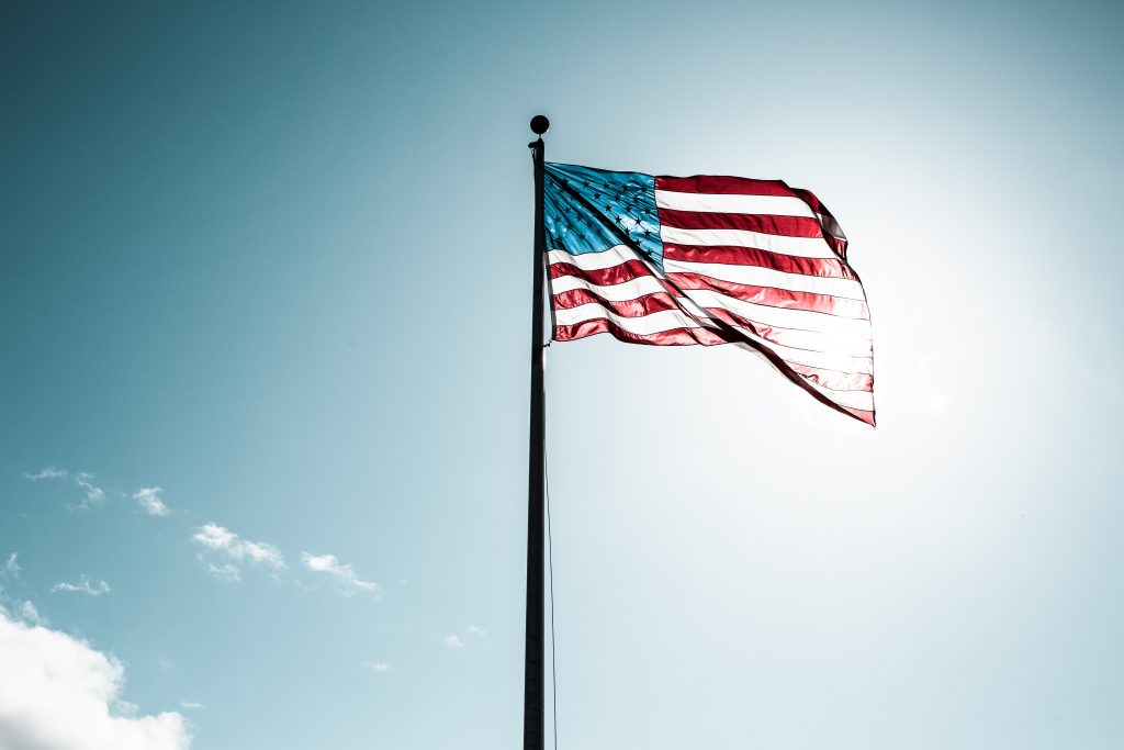 Blue sky as background. American flag front and center of image. 